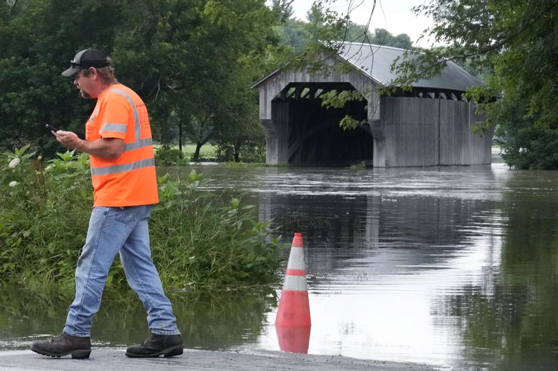 Jody Tanner, of the Vermont Transportation Agency, talks with co-workers at a high water point of the Lamoille River along Route 15 after remnants of Hurricane Beryl caused flooding, Thursday, July 11, 2024, in Cambridge, Vt. At rear is the Gates Farm Covered Bridge. (AP Photo/Charles Krupa)