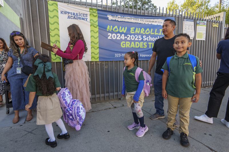 Roberto Garcia waits to sign in his children, Lily, 7, center, and Jack, 9, for their first day of school in East Los Angeles on Wednesday, Aug. 14, 2024. (AP Photo/Damian Dovarganes)