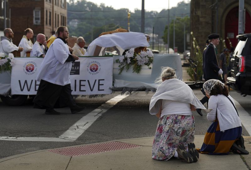 Catholics kneel as the Eucharist passes in procession in downtown Steubenville, Ohio, Friday, June 21, 2024. This and other weekend events were part of the National Eucharistic Pilgrimage, which will conclude at the National Eucharistic Congress in Indianapolis in mid-July, the first held in more than 80 years. (AP Photo/Jessie Wardarski)