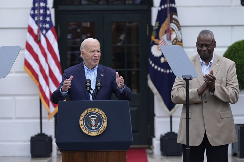 President Joe Biden, left, standing with Defense Secretary Lloyd Austin, right, speaks to active-duty military service members and their families during a Fourth of July celebration and barbecue on the South Lawn of the White House in Washington, Thursday, July 4, 2024. (AP Photo/Susan Walsh)
