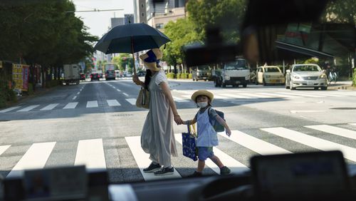 FILE - A pedestrian crossing a street with a child is seen through a taxi window in Tokyo, Monday, July 19, 2021. Japan’s birth rate fell to a new low for the eight straight year in 2023, according to Health Ministry data released on Wednesday, June 5, 2024. (AP Photo/David Goldman, File)