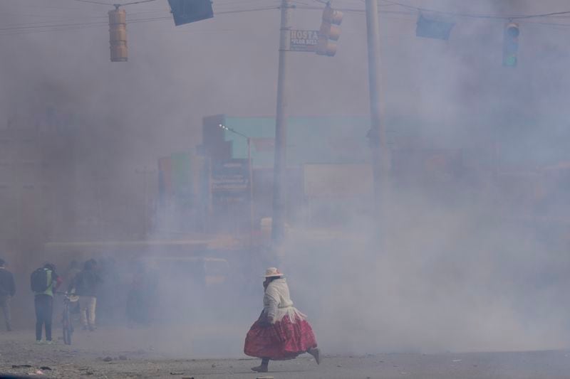 A woman runs through tear gas thrown by police during clashes between supporters of former President Evo Morales and current President Luis Arce in El Alto, Bolivia, Sunday, Sept. 22, 2024. (AP Photo/Juan Karita)