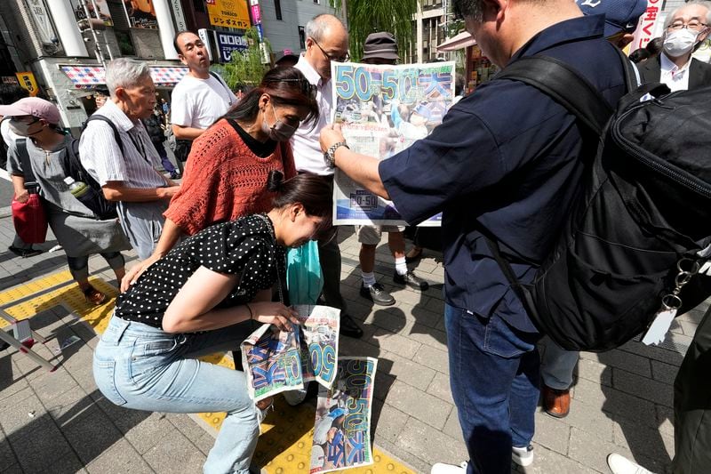 Pedestrians try to obtain an extra edition of the Sports Hochi newspaper reporting on the Los Angeles Dodgers' Shohei Ohtani becoming the first player in major league history with 50 home runs and 50 stolen bases in a season, Friday, Sept. 20, 2024, in Tokyo. (AP Photo/Eugene Hoshiko)