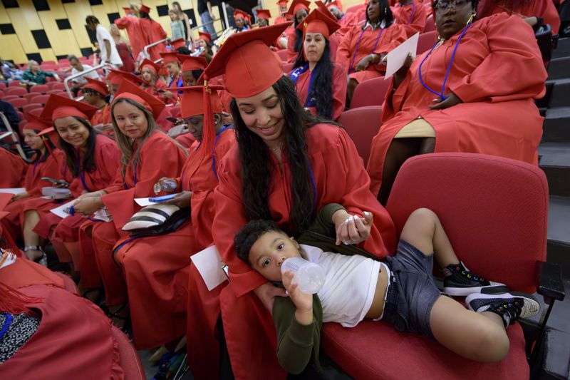 Litzy Moreno helps her son, Liam Ayala, 2, with a bottle before receiving her high school equivalency (HiSET) diploma during a graduation ceremony for the Youth Empowerment Project (YEP) in New Orleans, Thursday, June 27, 2024. YEP is a New Orleans-based non-profit organization which received money from the NBA Foundation program. (AP Photo/Matthew Hinton)