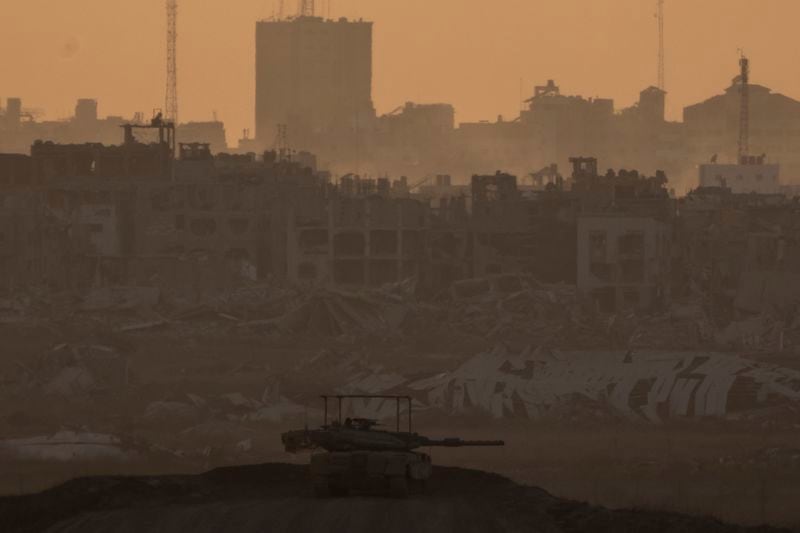 An Israeli tank is seen near the Israeli-Gaza border, with destroyed buildings in the back in the Gaza Strip, as seen from southern Israel, Wednesday, Aug. 21, 2024. (AP Photo/Leo Correa)