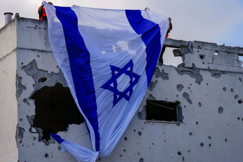 Municipality workers hang an Israeli flag over a damaged building that was hit by a rocket fired from Lebanon, in Kiryat Bialik, northern Israel, on Sunday, Sept. 22, 2024. (AP Photo//Ariel Schalit)