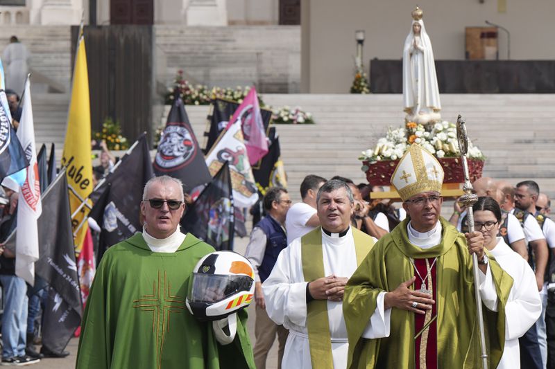 A priest carrying a Portuguese National Republican Guard motorcyclist helmet walks ahead of the Our Lady of Fatima statue in a procession closing the IX Pilgrimage of the Blessing of Helmets at the Roman Catholic holy shrine of Fatima to attend, in Fatima, Portugal, Sunday, Sept. 22, 2024. (AP Photo/Ana Brigida)