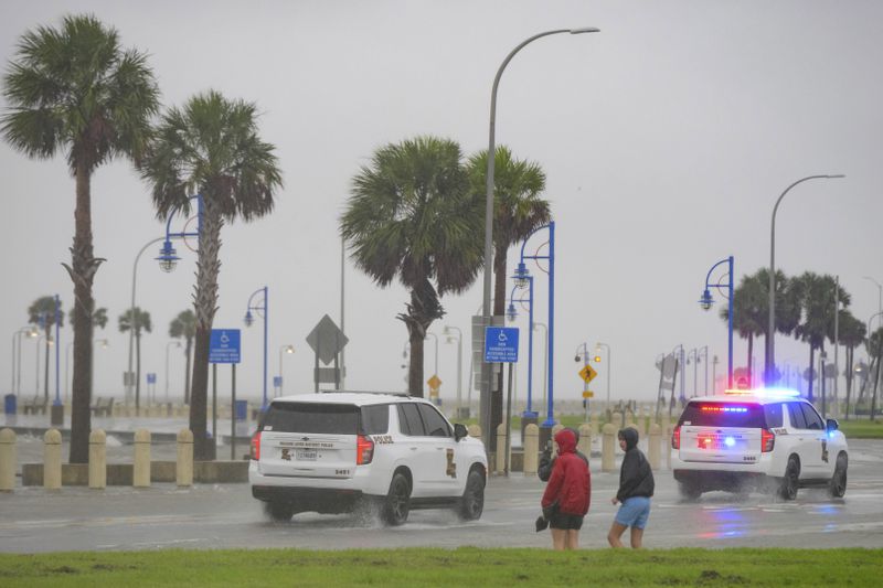 Cameron Henry, left, Owen Henry, and Stone Ridgeway, watch as Orleans Levee District Police patrol as rain and wind builds up from Hurricane Francine on Lakeshore Drive along Lake Ponchartrain in New Orleans, Wednesday, Sept. 11, 2024. (AP Photo/Matthew Hinton)