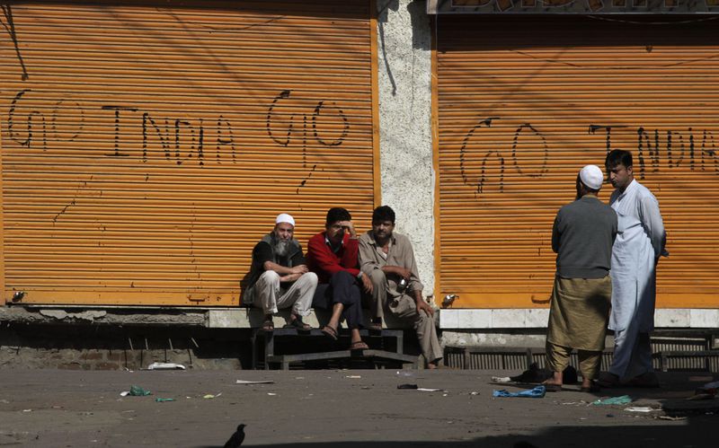 Kashmiris sit outside closed shops painted with graffiti during a curfew in central Srinagar, India, Thursday, Sept. 16, 2010. (AP Photo/Dar Yasin, File)