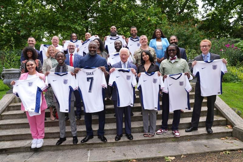 King Charles III centre with Idris Elba, centre left,and young people hold England football team shirts in support of the England football team as they attend an event for The King's Trust to discuss youth opportunity, at St James's Palace in central London, Friday July 12, 2024. The King and Mr Elba, an alumnus of The King's Trust (formerly known as The Prince's Trust), are meeting about the charity's ongoing work to support young people, and creating positive opportunities and initiatives which might help address youth violence in the UK, as well as the collaboration in Sierra Leone between the Prince's Trust International and the Elba Hope Foundation. (Yui Mok/pool photo via AP)