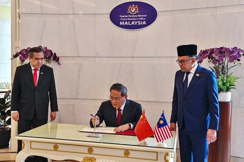 In this photo released by Malaysia's Department of Information, China's Premier Li Qiang, center, signs a guest book beside Malaysia Prime Minister Anwar Ibrahim, right, in Putrajaya, Malaysia, Wednesday, June 19, 2024. (Malaysia's Department of Information via AP)