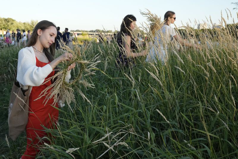 Ukrainian women collect ears of grain for their braids during a traditional Ukrainian celebration of Kupalo Night, in Warsaw, Poland, on Saturday, June 22, 2024. Ukrainians in Warsaw jumped over a bonfire and floated braids to honor the vital powers of water and fire on the Vistula River bank Saturday night, as they celebrated their solstice tradition of Ivan Kupalo Night away from war-torn home. (AP Photo/Czarek Sokolowski)