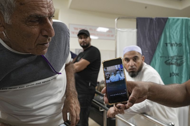 Friends and relatives show a phone with an image of Qaid Farhan Alkadi, 52, who was held hostage by Hamas militants in the Gaza Strip, as they stand at the Soroka Medical Center in Beersheba, Israel, Tuesday, Aug. 27, 2024. (AP Photo/Tsafrir Abayov)