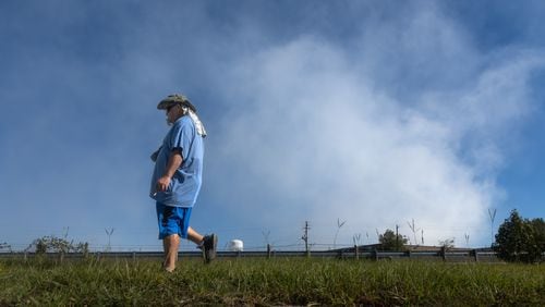 Darryl Shumake walks along Iris Drive at mid-morning Wednesday, Oct 2, 2024 as a large mile-long plume was still visible over Conyers as crews worked at the BioLab plant that caught on fire days earlier. But as the sun lifted above the horizon, so did the shelter-in-place order for Rockdale County residents. Those living nearby have been advised to stay inside every evening through early morning until Friday. (John Spink/AJC)