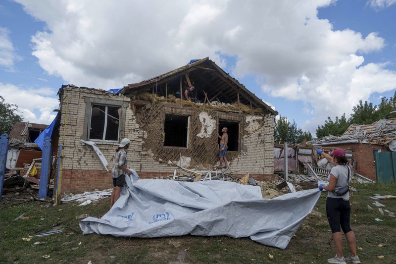 People cover a roof with tarps after their house was hit by Russian airstrike near the Russian-Ukrainian border in Sumy region, Ukraine, Thursday, Aug. 15, 2024. (AP Photo/Evgeniy Maloletka)