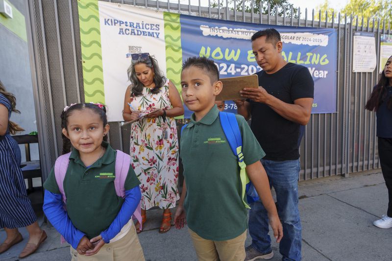 Roberto Garcia, right, signs in his children, Lily, 7, center, and Jack, 9, for their first day of school in East Los Angeles on Wednesday, Aug. 14, 2024. (AP Photo/Damian Dovarganes)