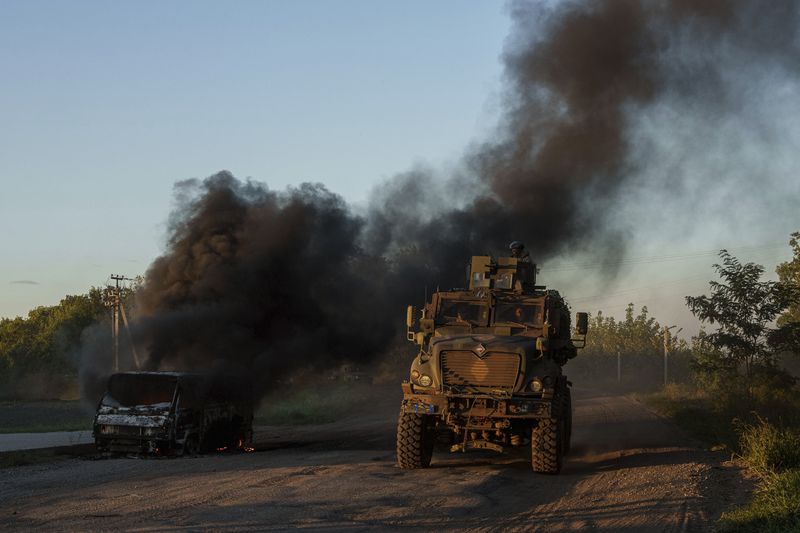 A Ukrainian armoured military vehicle travels past a burned car near the Russian-Ukrainian border, Sumy region, Ukraine, Wednesday, Aug. 14, 2024. (AP Photo/Evgeniy Maloletka)