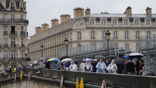 Pedestrians make their way across a sidewalk opened to foot traffic on the Pont Royal, or Royal Bridge, along grandstands used in the opening ceremonies, at the 2024 Summer Olympics, Saturday, July 27, 2024, in Paris, France. (AP Photo/Rebecca Blackwell)