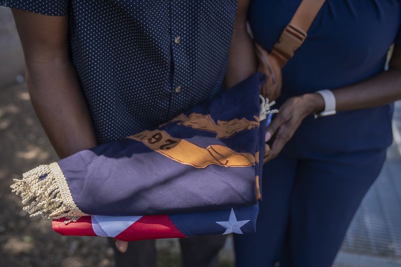 Associated Press reporter Darren Sands, left, and his wife Jummy Olabanji Sands, right, hold a U.S. flag and a flag from the 26th United States Colored Infantry, which his great-great-great-great grandfather Hewlett Sands served in, at the African American Civil War Memorial during Juneteenth commemorations on Wednesday, June 19, 2024, in Washington. (AP Photo/Mark Schiefelbein)