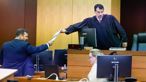 Baxter Drennon (left), a lawyer representing the Republican National Committee, hands documents to Fulton County Superior Court Judge Robert McBurney on Tuesday during a trial brought by the Georgia Democratic Party challenging the State Election Board’s certification rule. (Miguel Martinez/AJC)