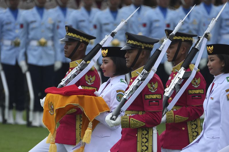 A bearer is escorted by members of a honor guard as she carries the national Red-White flag to be hoisted during the ceremony marking Indonesia's 79th anniversary of independence at the new presidential palace in its future capital of Nusantara, a city still under construction on the island of Borneo, Saturday, Aug. 17, 2024. (AP Photo/Achmad Ibrahim)