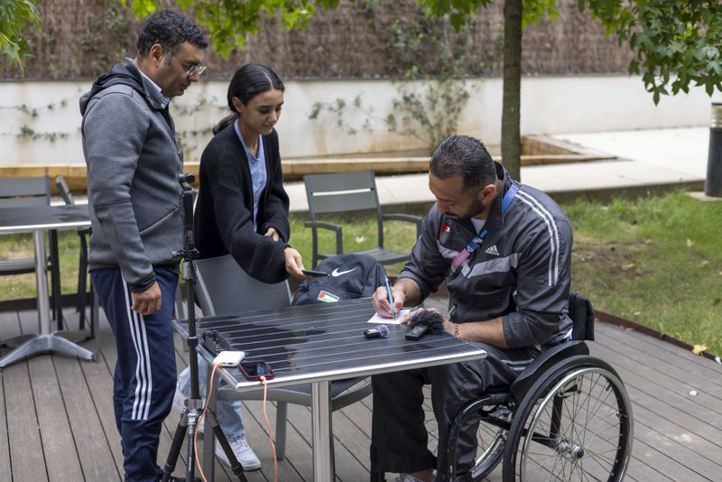 Fadi Aldeeb, the only Palestinian athlete at the Paralympic Games, signs an autograph for a young fan during an interview with The Associated Press in Paris, Tuesday, Sept. 3, 2024. (AP Photo/Ciaran Fahey)