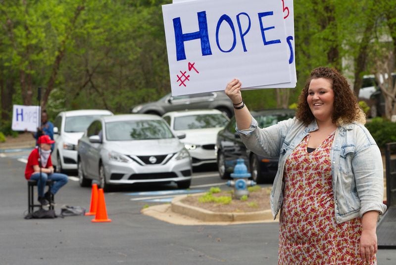 Summer Osbon holds up a sign as her father, Pastor Shell Osbon, talks to the crowd during the Drive-in church service at the Life Church Smyrna Assembly of God Sunday, April 5, 2020.  STEVE SCHAEFER / SPECIAL TO THE AJC