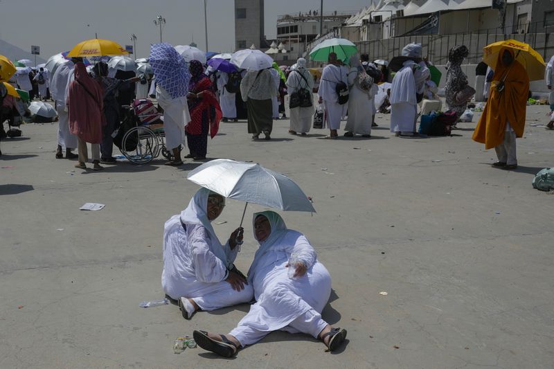 Two muslim pilgrim women share umbrella to protect themself from sun near pillars in the symbolic stoning of the devil, the last rite of the annual hajj, in Mina, near the holy city of Mecca, Saudi Arabia, Sunday, June 16, 2024. Masses of pilgrims on Sunday embarked on a symbolic stoning of the devil in Saudi Arabia. The ritual marks the final days of the Hajj, or Islamic pilgrimage, and the start of the Eid al-Adha celebrations for Muslims around the world. (AP Photo/Rafiq Maqbool)