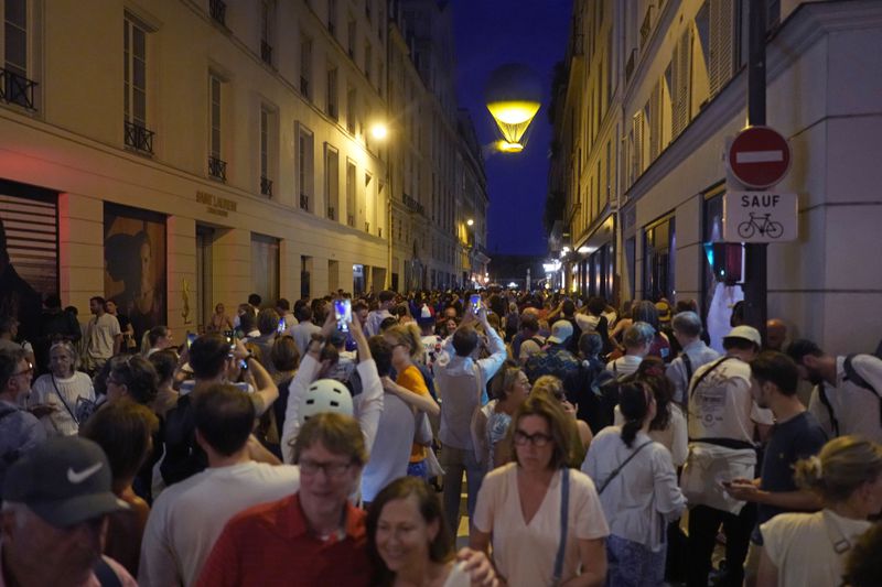 HOLD FOR STY of DIANE JEANTET****FILE-People gather in a street to watch the Olympic cauldron at the Tuileries Garden during the 2024 Summer Olympics, Tuesday, Aug. 6, 2024, in Paris, France. With the Olympic and Paralympic Games officially over, time has come to run the numbers. And in the service industry, many say reality has far from matched expectations, recording instead one of their worst summers ever. (AP Photo/Charlie Riedel, File)