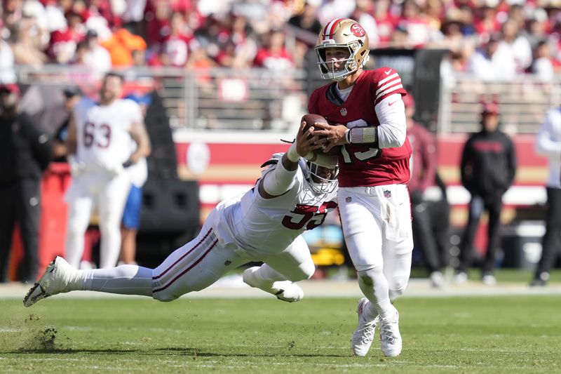 San Francisco 49ers quarterback Brock Purdy, right, scrambles away from Arizona Cardinals defensive tackle Dante Stills during the second half of an NFL football game in Santa Clara, Calif., Sunday, Oct. 6, 2024. (AP Photo/Godofredo A. Vásquez)