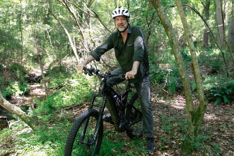 Joe Peery poses for a photo on his mountain bike on a trail he created close to Intrenchment Park in DeKalb County on Tuesday, August 1, 2023.  Peery, along with other members of the community are calling on DeKalb CEO Michael Thurmond to reopen Intrenchment Park for recreational and transportation purposes. (Natrice Miller/ natrice.miller@ajc.com)