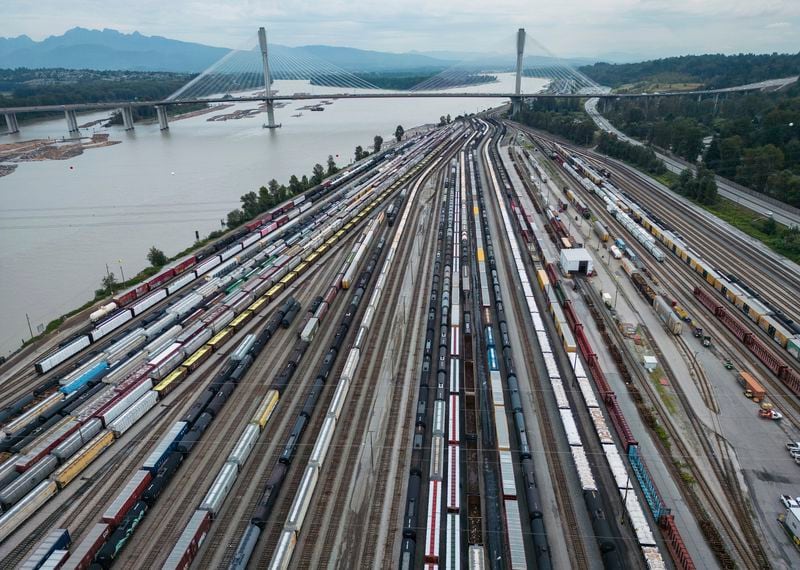 Train cars are seen on the tracks in an aerial view at Canadian National Rail's Thornton Yard as the Port Mann Bridge spans the Fraser River and trucks transport cargo containers on the highway in Surrey, British Columbia, Canada, Thursday, Aug. 22, 2024. (Darryl Dyck/The Canadian Press via AP)