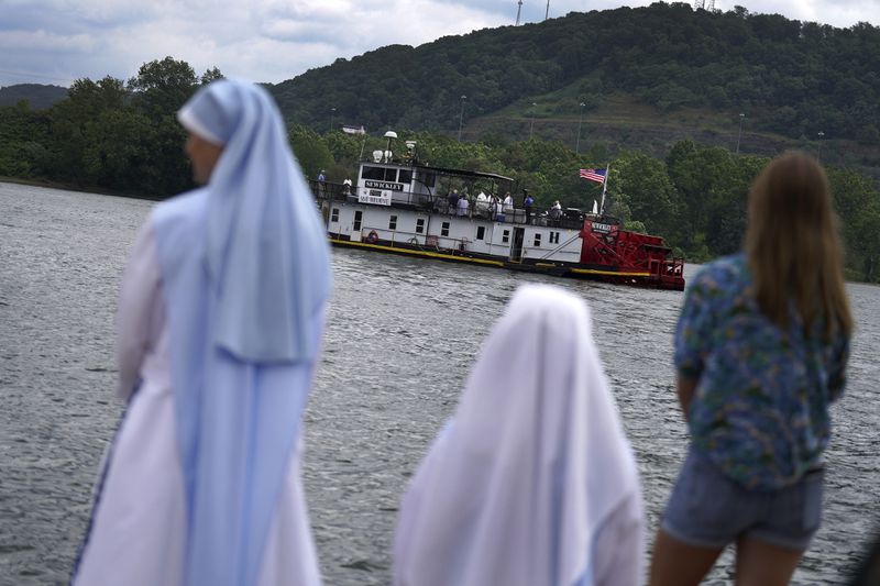 Catholics stand on the edge of the Ohio River watching the Eucharist move down the Ohio River headed for Wheeling, W.Va., Sunday, June 23, 2024, in Steubenville, Ohio. (AP Photo/Jessie Wardarski)