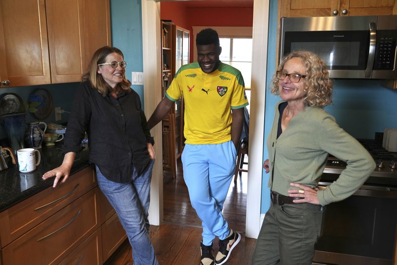 Cabrel Ngougou, center, a refugee from Cameroon, talks with his sponsors Lori Ostlund, left, and Anne Raeff in their home in San Francisco Tuesday, Sept. 17, 2024. (AP Photo/Terry Chea)