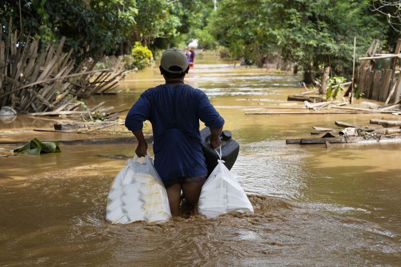 Local residents carrying food wade through a flooded road in Naypyitaw, Myanmar, Saturday, Sept. 14, 2024. (AP Photo/Aung Shine Oo)