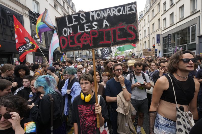 A demonstrator holds a poster which reads 'the monarchs were beheaded' during a protest, responding to a call from the far-left party who criticized as a power grab the president's appointment of a conservative new prime minister, Michel Barnier, in Paris, France, Saturday, Sept. 7, 2024. (AP Photo/Michel Euler)