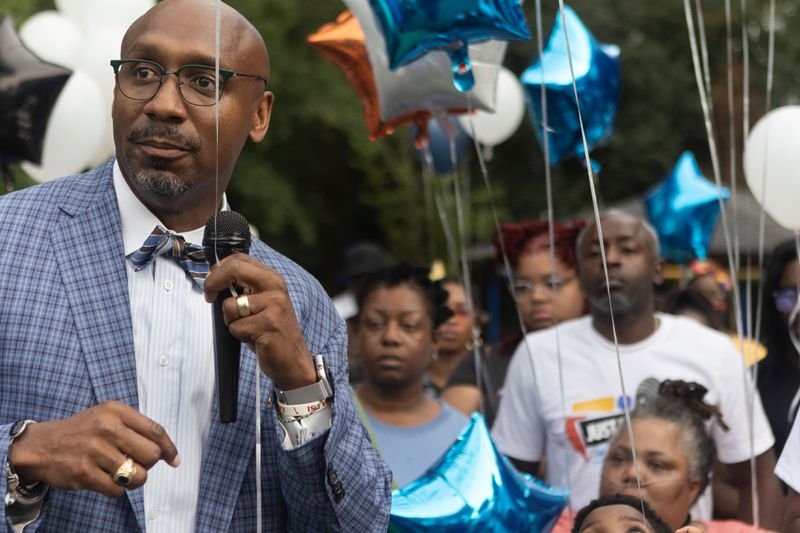 Attorney Mawuli Davis talks to family members and friends of Johnny Hollman during a vigil and balloon release Tuesday at Dr. Mary Shy Scott Park. 