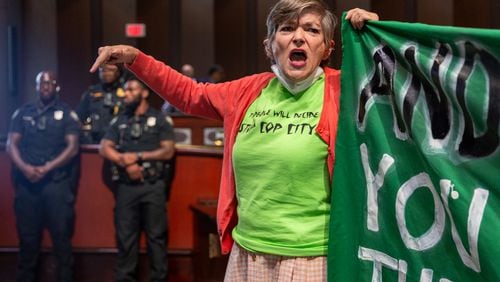 Priscilla Smith holds a banner as opponents of the under-construction law enforcement training center known to some as Cop City disrupt the City Council meeting at City Hall in Atlanta on Monday, September 16, 2024. It’s been one year since opponents submitted a petition to force a referendum to block the project. (Arvin Temkar / AJC)