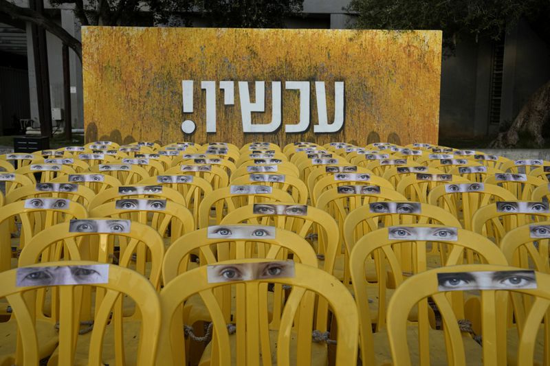 Chairs representing hostages held by Hamas militants in the Gaza Strip, are displayed beneath the Hebrew word, "now,"ahead of a weekly protest by families of the hostages and their supporters to demand their release, in Tel Aviv, Israel, Saturday, Aug. 17, 2024. (AP Photo/Tsafrir Abayov)