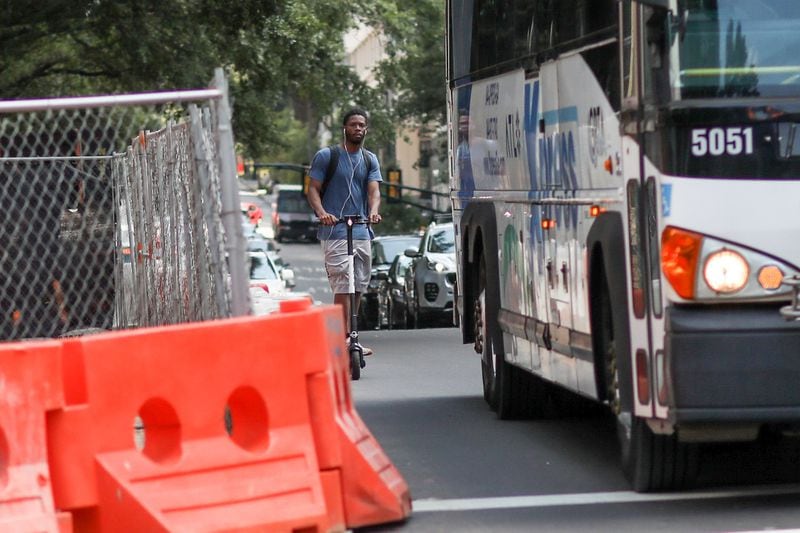 A man rides a scooter while sharing a lane with a bus on West Peachtree Street on Wednesday, July 24, 2019, in Atlanta, near where e-scooter rider William Alexander was fatally crushed by a bus a week prior. BRANDEN CAMP/SPECIAL