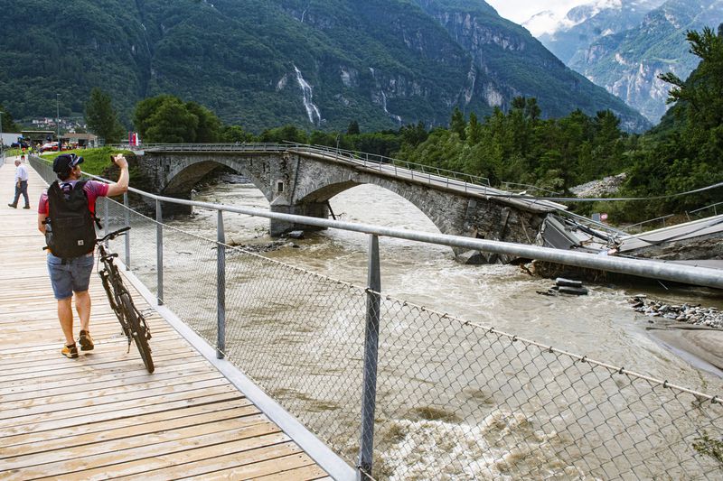 A man takes a photo of the collapsed Visletto bridge between Visletto and Cevio, in the Maggia Valley, southern Switzerland, Sunday June 30, 2024. Authorities say weekend storms in Switzerland and northern Italy caused extensive flooding and landslides, leaving at least four people dead. Storms and heavy rain affected southern and western Switzerland on Saturday and overnight. (Samuel Golay/Ti-Press/Keystone via AP)