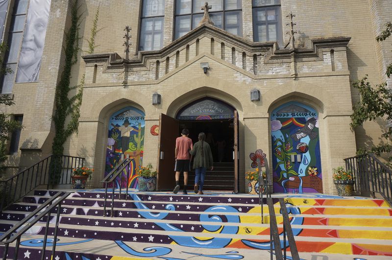 Congregants walk into Iglesia Luterana San Pablo in Minneapolis for Sunday service on Sept. 8, 2024. A mural was recently completed on the steps and main entrance of the Lutheran church, combining symbols of its historical Swedish heritage with its function today as a center for the Latino community. (AP Photo/Giovanna Dell'Orto)