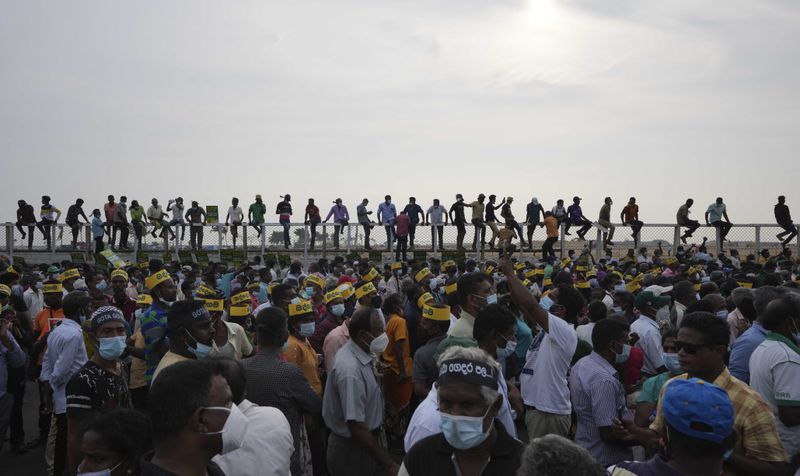 Supporters of Sri Lanka's main opposition sit on the fence of the Chinese owned Port City project as they gather to protest and demand President Gotabaya Rajapaksa's resignation in Colombo, Sri Lanka, Tuesday, March 15, 2022. (AP Photo/Eranga Jayawardena, File)