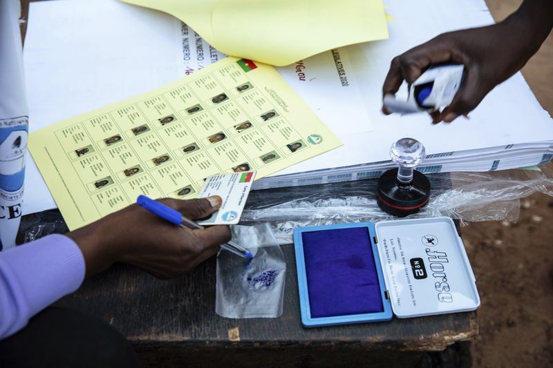 FILE - Election officials check identification papers of people who lined up to vote in Burkina Faso's presidential and legislative elections as polling stations open in Ouagadougou, Sunday, Nov. 22, 2020. (AP Photo/Sophie Garcia, File)