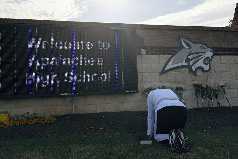 A person kneels in front of flowers that are placed outside the entrance to Apalachee High School on Thursday, Sept. 5, 2024 in Winder, Ga., a day after deadly shootings at the school. (AP Photo/Charlotte Kramon)