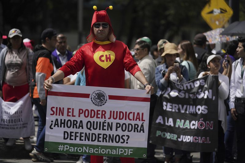 A demonstrator in a Chapulín Colorado costume holds the sign "Without judicial power, who will be able to defend us now?" outside the Senate to protest the judicial reform bill in Mexico City, Thursday, Sept. 5, 2024, the day after Congress passed legislation that would require all judges to stand for election. (AP Photo/Felix Marquez)