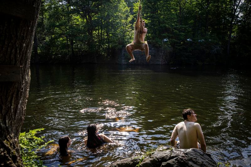 Athena Bean, from left, Emily Champagne and Tyler Lippe sit in the water, Tuesday, June 18, 2024, while a man swings out over the Saco River in Buxton, Maine. Hot weather is predicted until the end of the week. (Troy R. Bennett/The Bangor Daily News via AP)