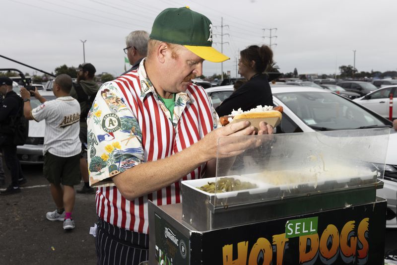 Mike Davie prepares a hot dog outside the Oakland Coliseum before the Athletics final home baseball game at the Coliseum against the Texas Rangers, Thursday, Sept. 26, 2024, in Oakland, Calif. (AP Photo/Benjamin Fanjoy)