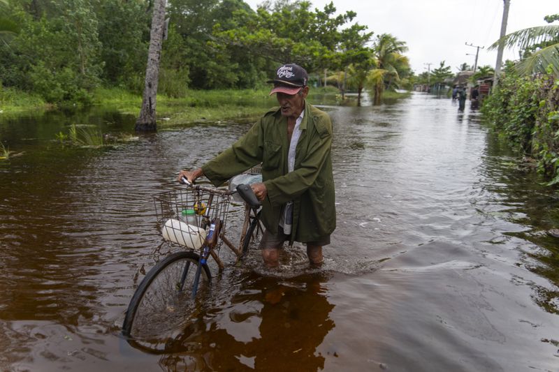 A man pushes his bicycle through a flooded street after Hurricane Helene passed through Guanimar, Artemisa province, Cuba, Wednesday, Sept. 25, 2024. (AP Photo/Ramon Espinosa)