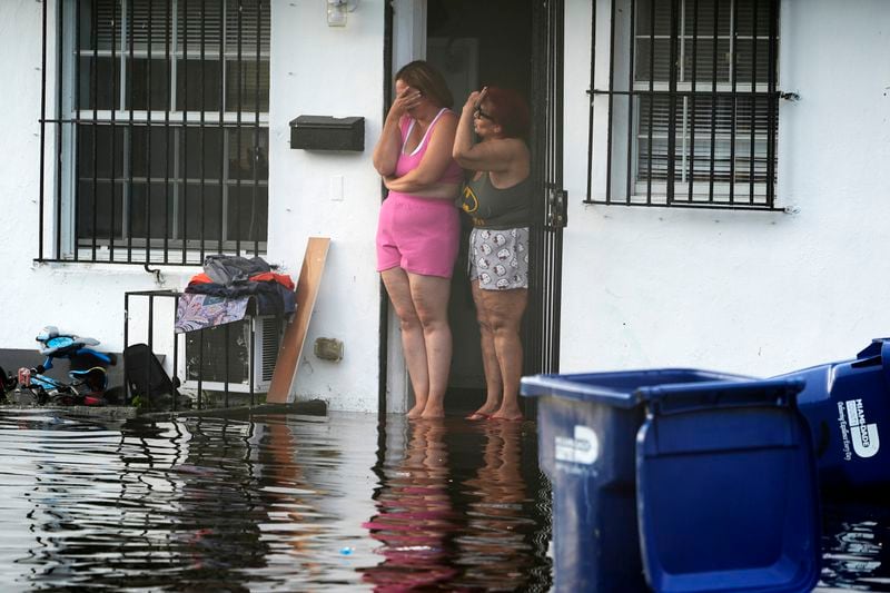 Two women react as they see flooding on their street, Thursday, June 13, 2024, in North Miami, Fla. A tropical disturbance has brought a rare flash flood emergency to much of southern Florida. Floridians prepared to weather more heavy rainfall on Thursday and Friday. (AP Photo/Marta Lavandier)